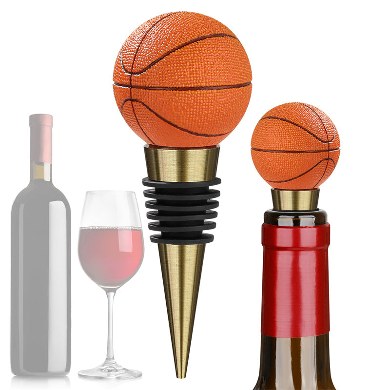 A realistic miniature basketball wine bottle stopper with a textured orange surface and gold metal cone base, isolated on a clear white background.
